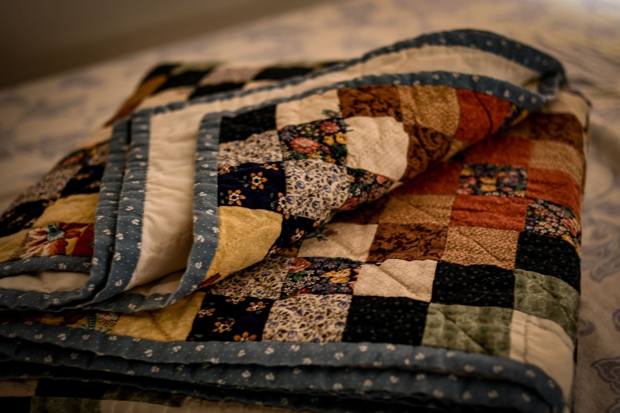 A folded quilt patchwork on a bed for Conscious by Chloé