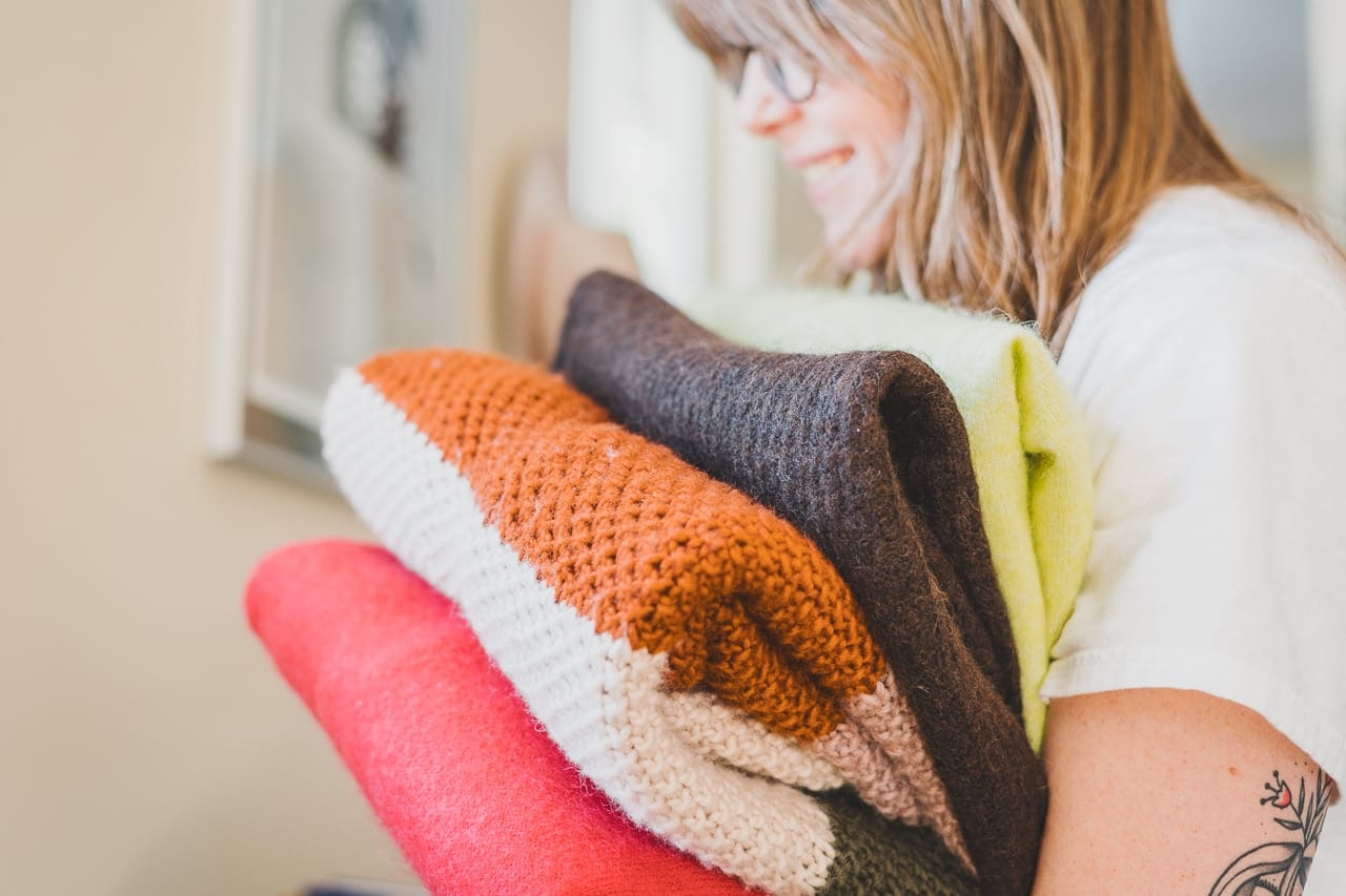 Woman Holding a Pile of Colorful Sweaters by Conscious by Chloé